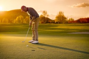 A Man putting a ball in the golf ground on a beautiful sunrise.