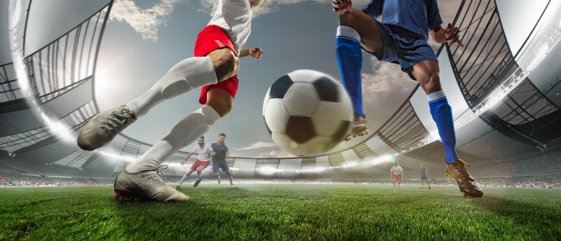 In a football ground two teams were playing, two team members kicking the football wearing boot and team jersy.